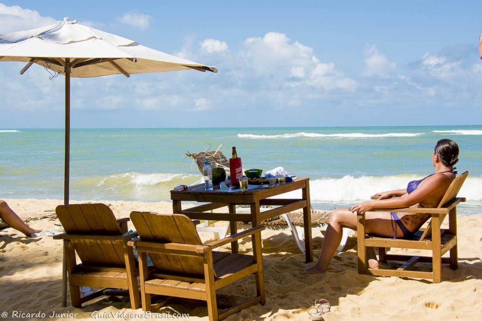 Imagem de uma moça na mesa na praia admirando o mar maravilhoso da Praia do Rio Verde.